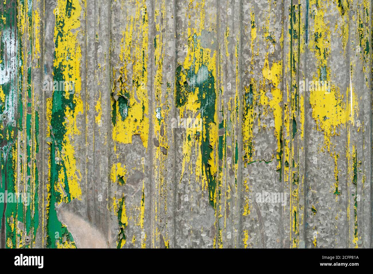 Ancienne clôture en fonte ondulée avec peinture verte et jaune qui s'écaille. Texture abstraite Banque D'Images