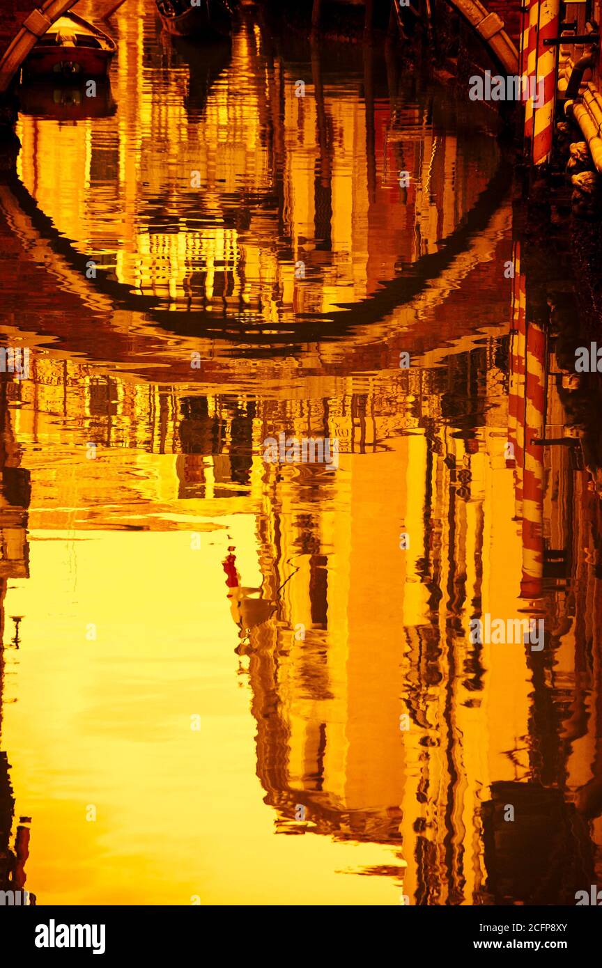 Réflexion de maisons et de petit pont dans l'eau d'un canal étroit. Venise (Italie). Mise au point sélective. Lumière dorée au coucher du soleil. Photo en tons. Banque D'Images