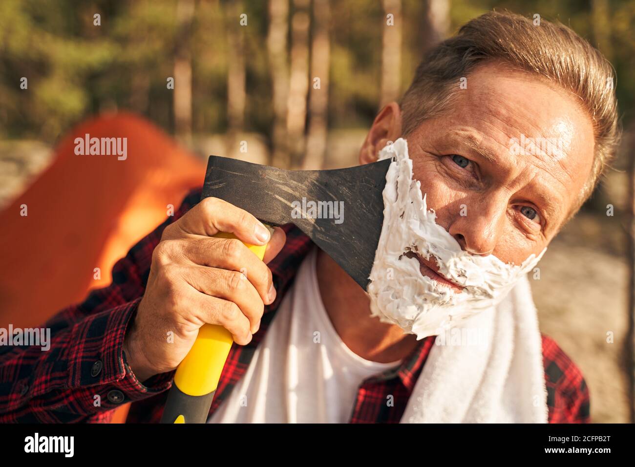 Un homme joyeux se raser la barbe avec une hache dans la nature Banque D'Images