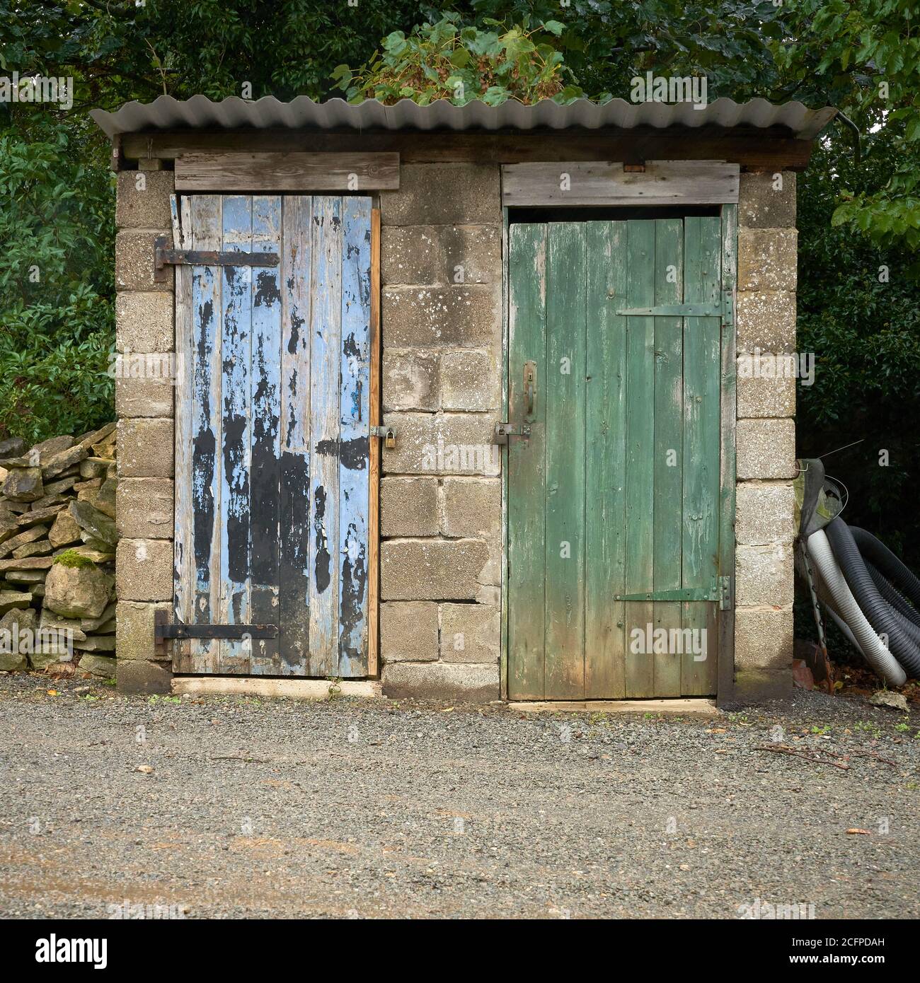 Hangar de blocs de brise avec 2 portes en bois altérées un vert et un toit en métal bleu et ondulé Banque D'Images