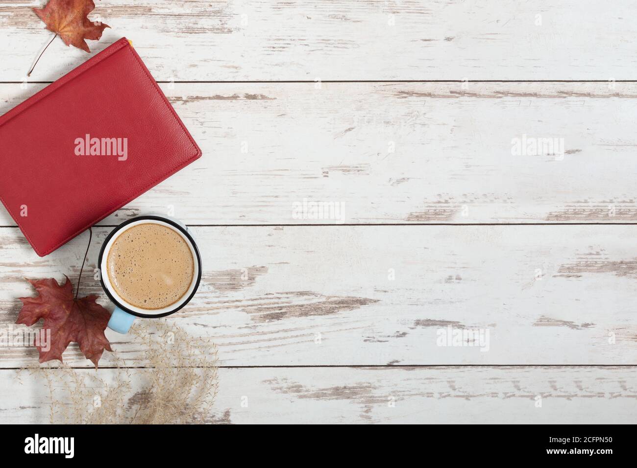 Tasse de café, livre et feuilles d'automne colorées sur fond de bois blanc vue du dessus. Composition d'automne. Banque D'Images