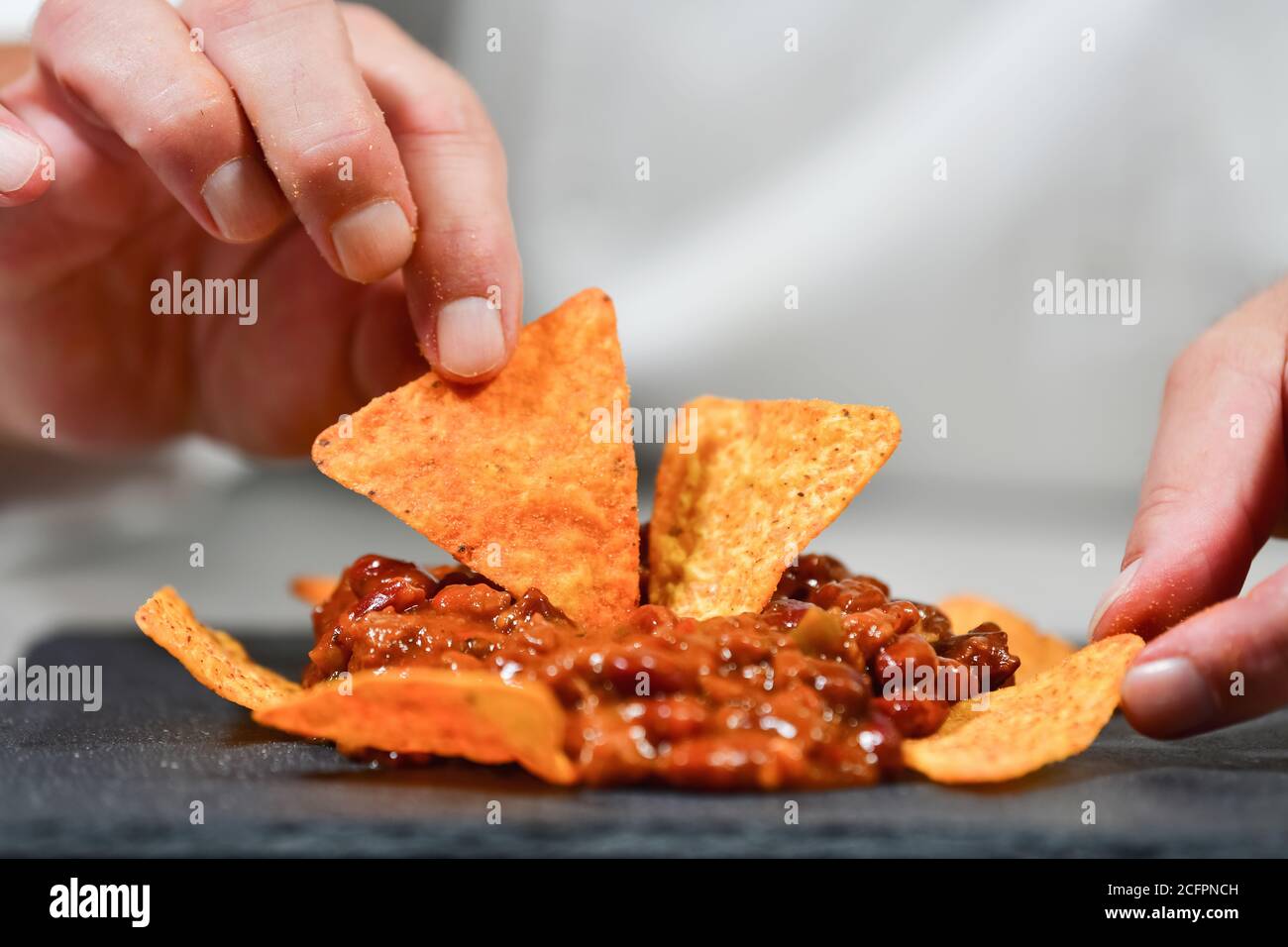 Gros plan sur les mains de sexe masculin en organisant de délicieux nachos avec du piment sur une plaque sombre Banque D'Images