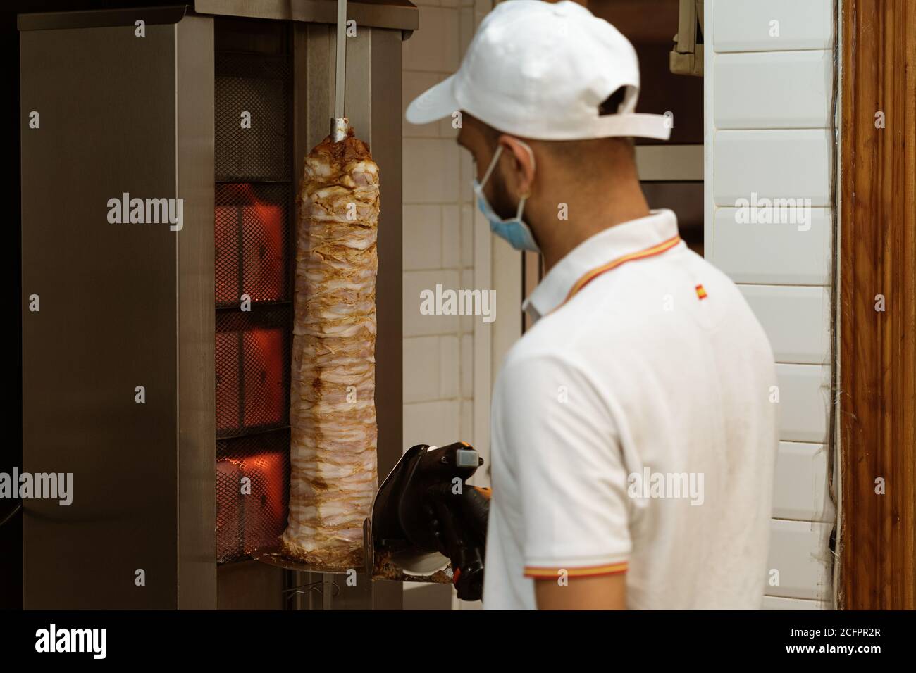 Chef en uniforme, coupant et préparant des kebabs de poulet et de beer de bœuf en utilisant un masque de prévention sur un stand de restauration rapide Banque D'Images