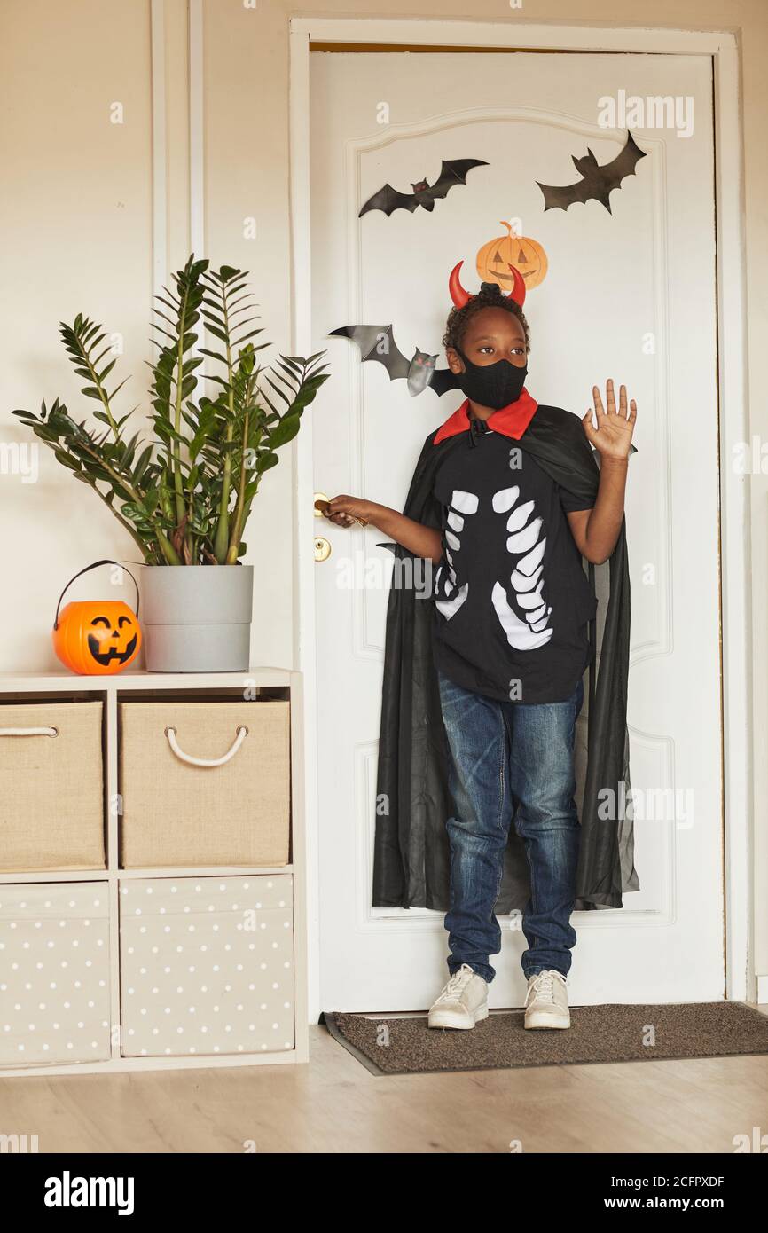 Un garçon afro-américain méconnaissable portant un costume de diable avec des cornes rouges et un masque noir sur le visage disant Au revoir à ses parents et allant à trick ou à traiter. Banque D'Images