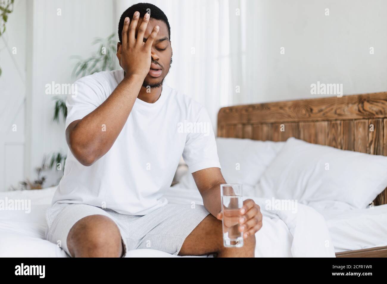 Un gars qui a le pendu en touchant la tête de la douleur assis dans le lit à l'intérieur Banque D'Images