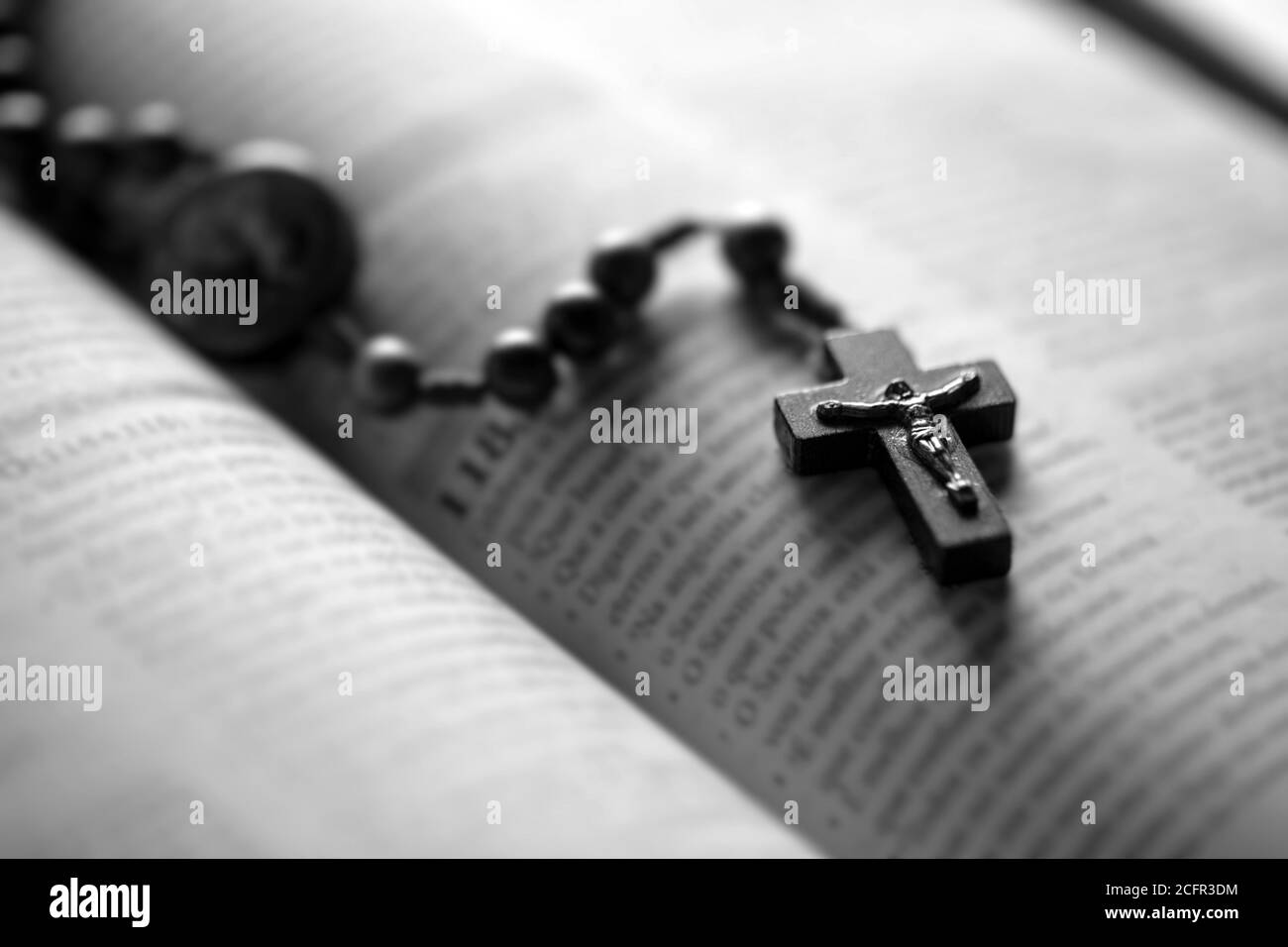 Crucifix en bois chrétien sur la bible ouverte, point de mire. Image de concept religieux, image en noir et blanc Banque D'Images