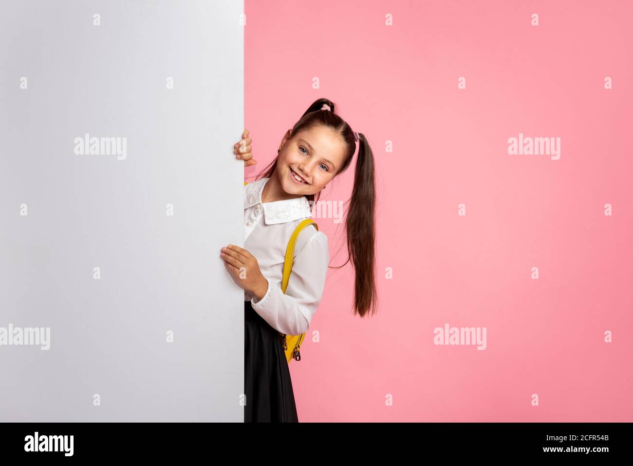 Prêt pour la leçon. Gaie écolière en uniforme sort avec un panneau d'affichage blanc Banque D'Images