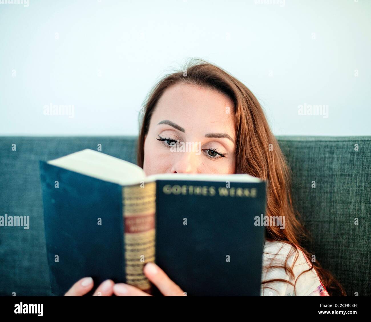 Femme lisant un livre sur un canapé Banque D'Images