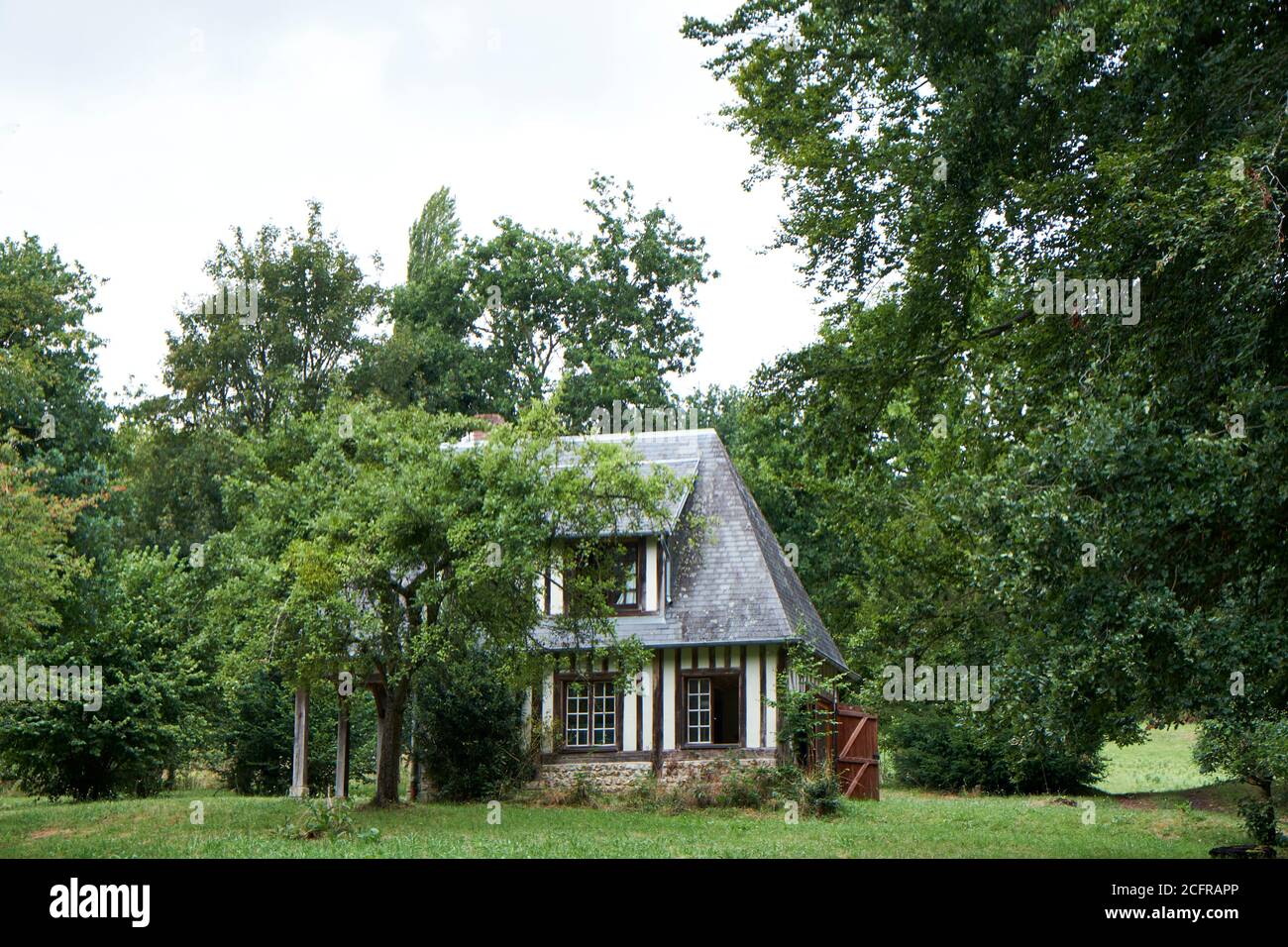 Petite maison normande indépendante à colombages avec toit en tuiles d'ardoise entouré par les arbres dans un jardin Banque D'Images