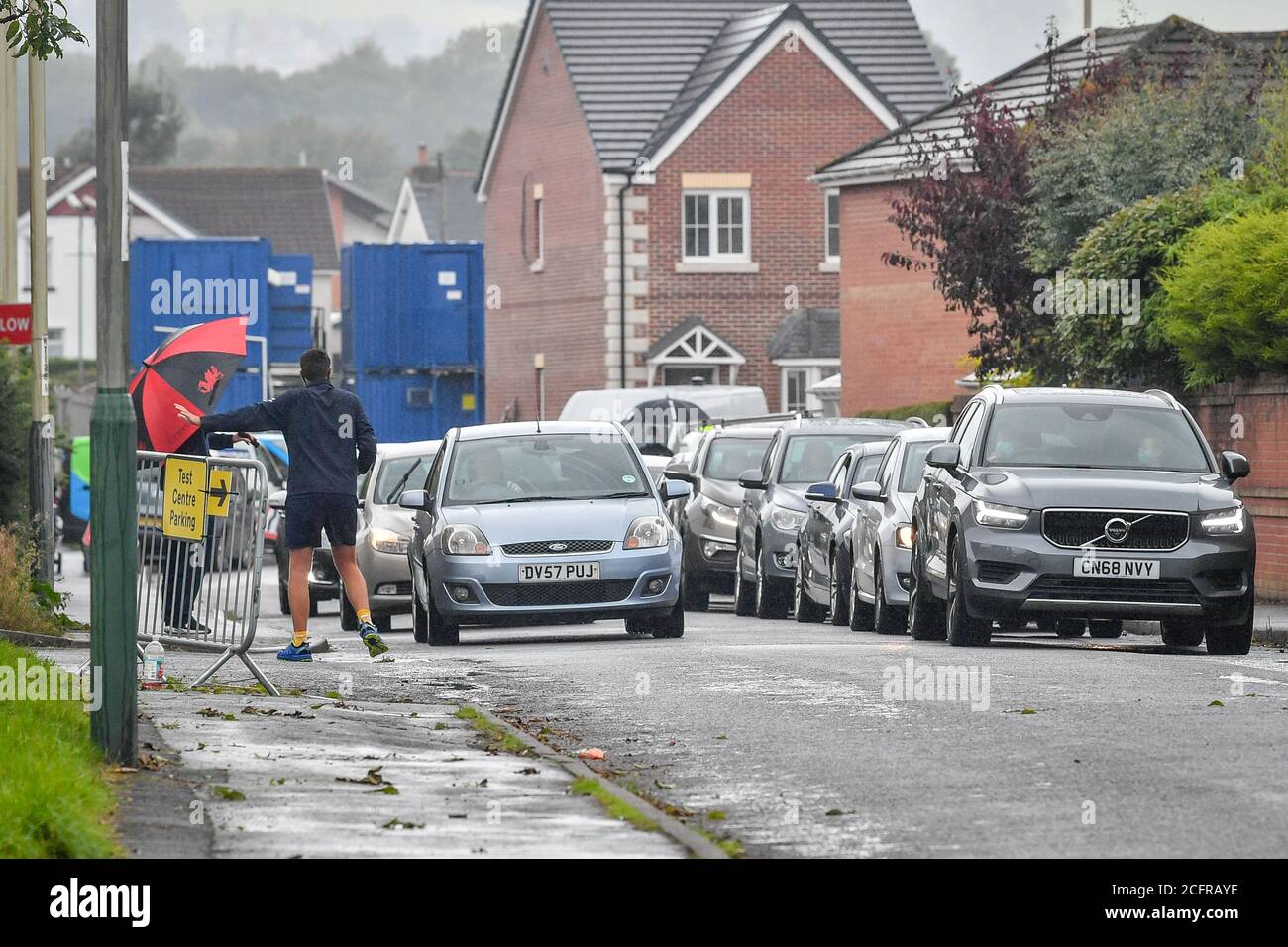 Une longue file d'attente de voitures est dirigée par un marshall avant d'accéder au centre d'essai du coronavirus au Caerphilly Leisure Centre, pays de Galles, qui a été mis en place pour répondre à des niveaux élevés de la demande suite à une augmentation des cas Covid dans le quartier. Banque D'Images