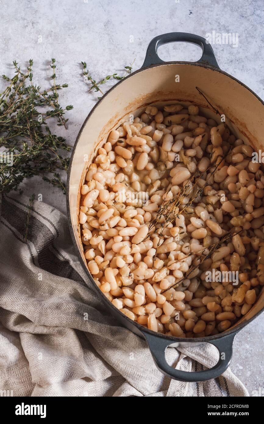 Pot de fève de cannellini vegan ragoût sur une table avec une serviette de thé en lin et un bouquet de frais thym Banque D'Images