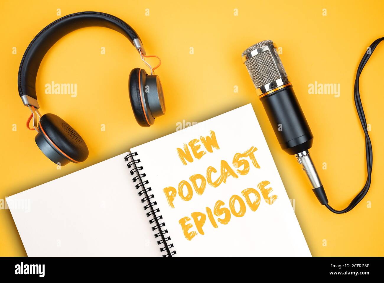 NOUVEAU texte D'ÉPISODE DE PODCAST sur le bloc-notes à côté des écouteurs et du microphone d'enregistrement, concept de podcasting sur fond orange Banque D'Images