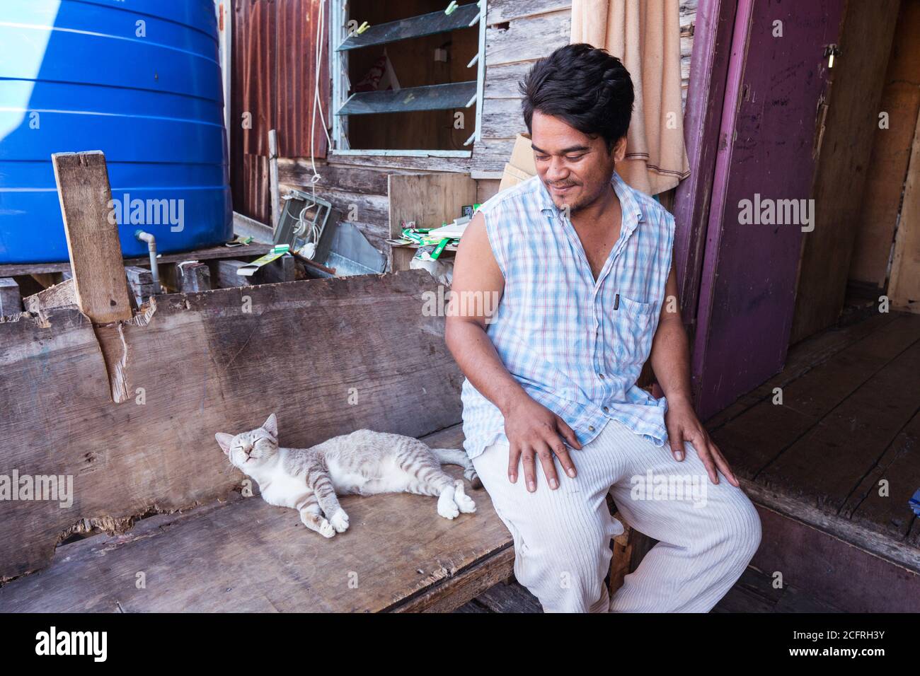 Kota Kinabalu / Malaisie - 13 janvier 2019: Travailleur migrant philippin assis à côté du chat dans sa maison en bois dans le village flottant Banque D'Images