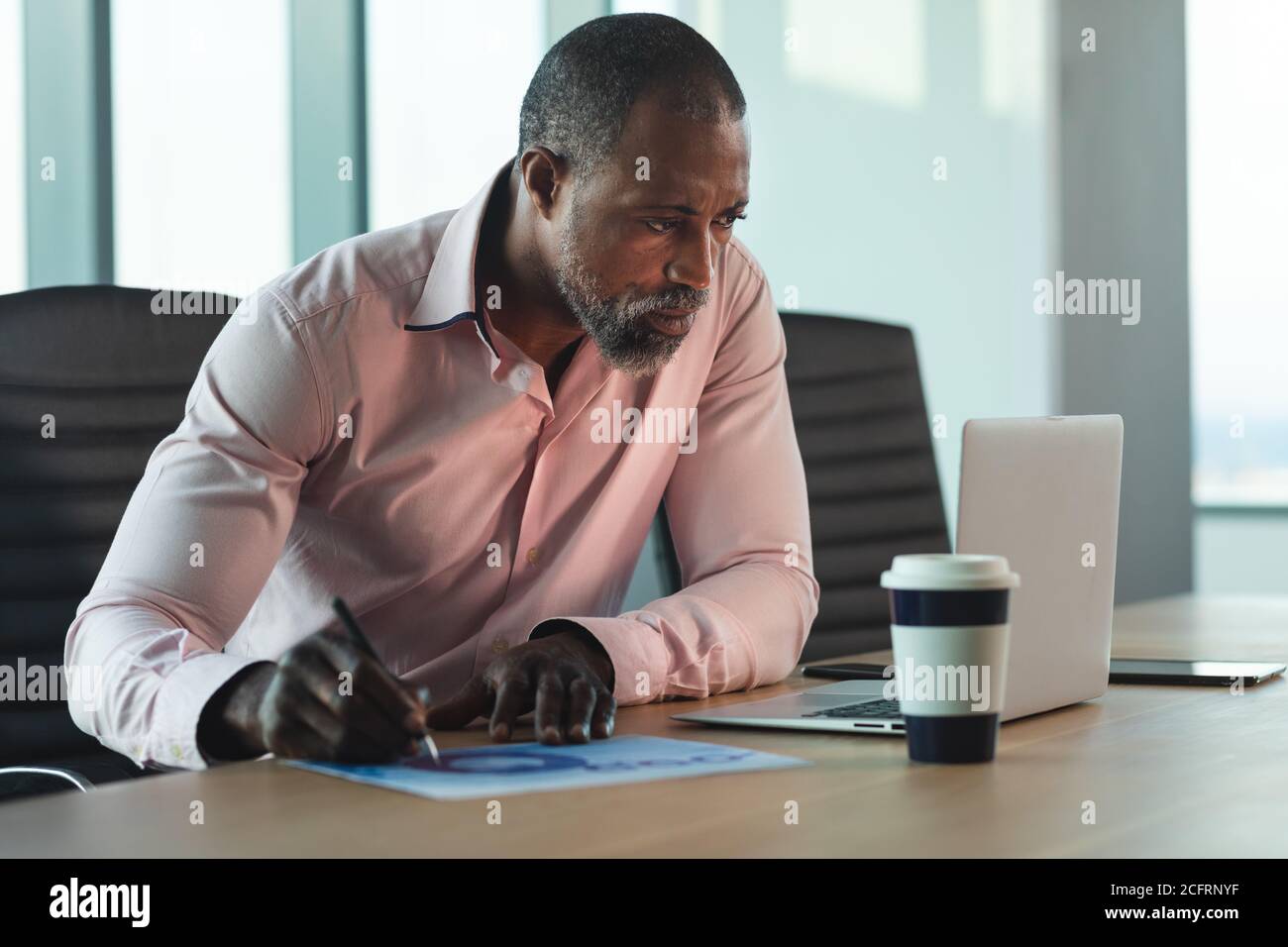 Homme d'affaires senior prenant des notes tout en se tenant à son ordinateur portable bureau moderne Banque D'Images