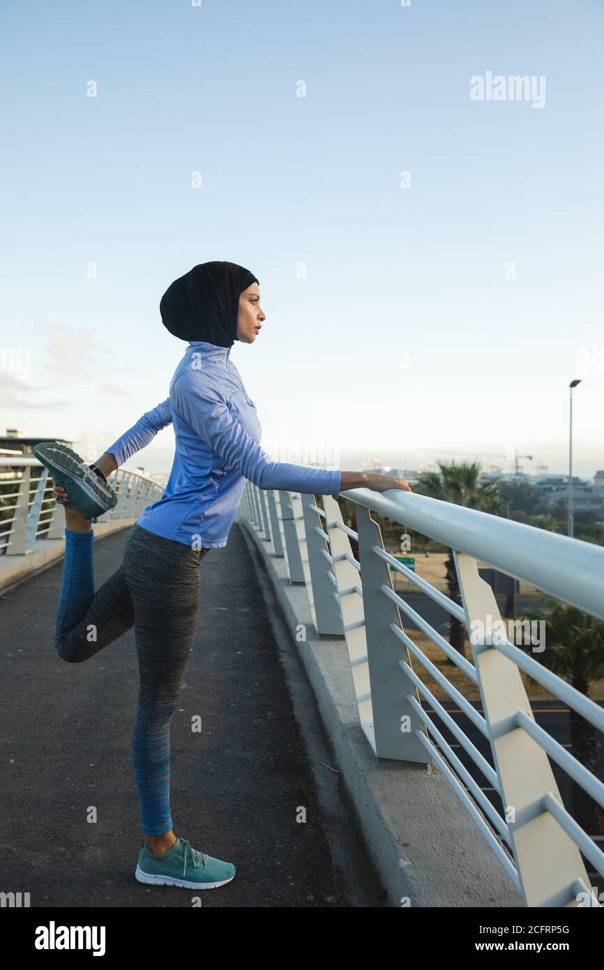 Femme en hijab effectuant un exercice d'étirement sur une passerelle Banque D'Images Femme en hijab effectuant un exercice d'étirement sur une passerelle Banque D'Images
