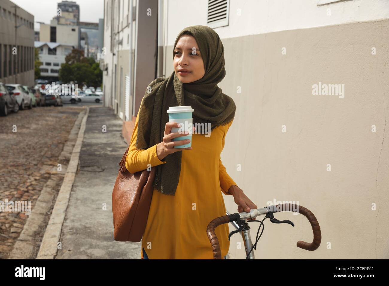 Femme tenant une tasse de café tout en marchant avec un vélo Banque D'Images Femme tenant une tasse de café tout en marchant avec un vélo Banque D'Images
