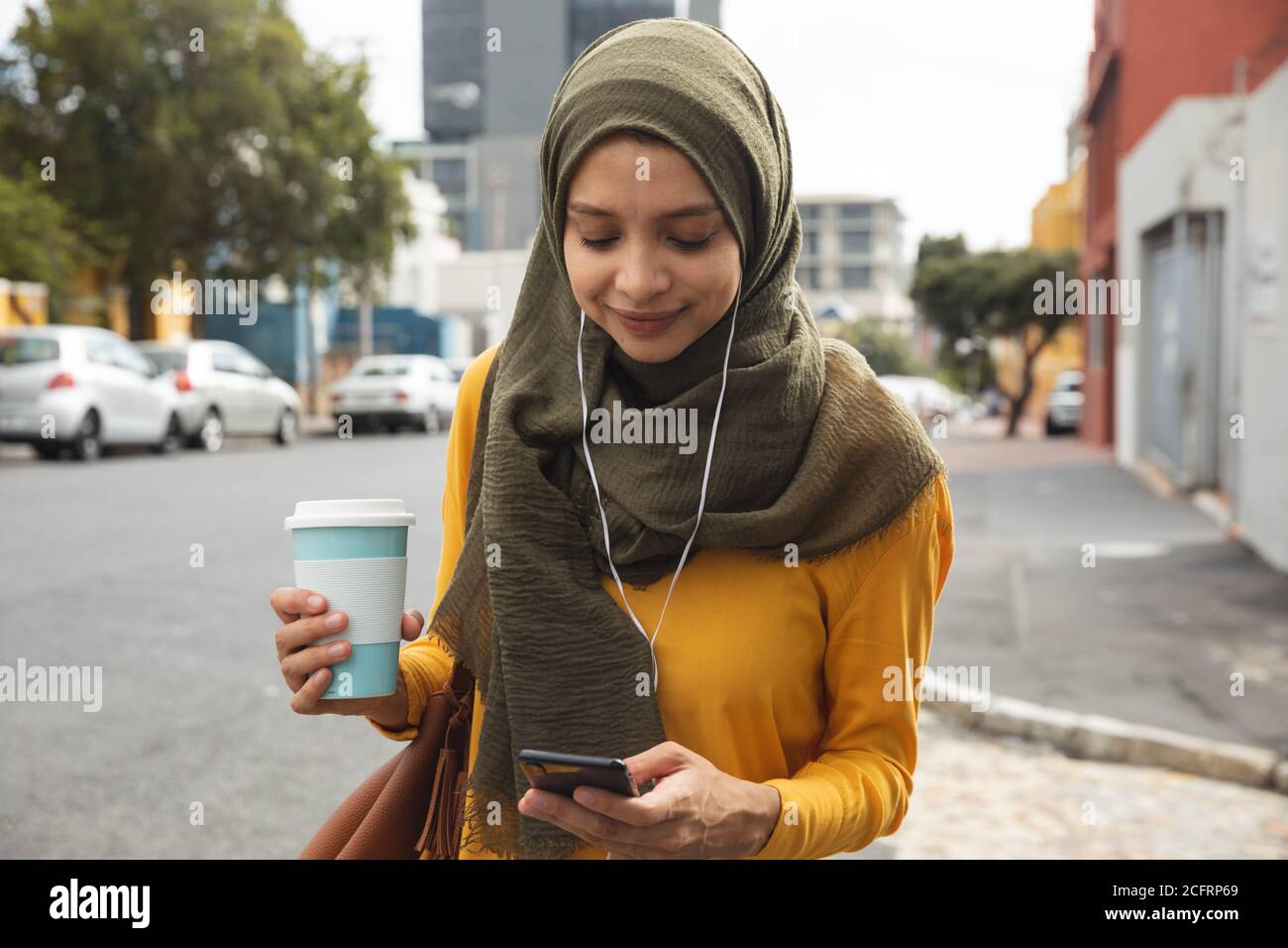 Femme en hijab avec une tasse de café utilisant un smartphone sur le rue Banque D'Images Femme en hijab avec une tasse de café utilisant un smartphone sur le rue Banque D'Images
