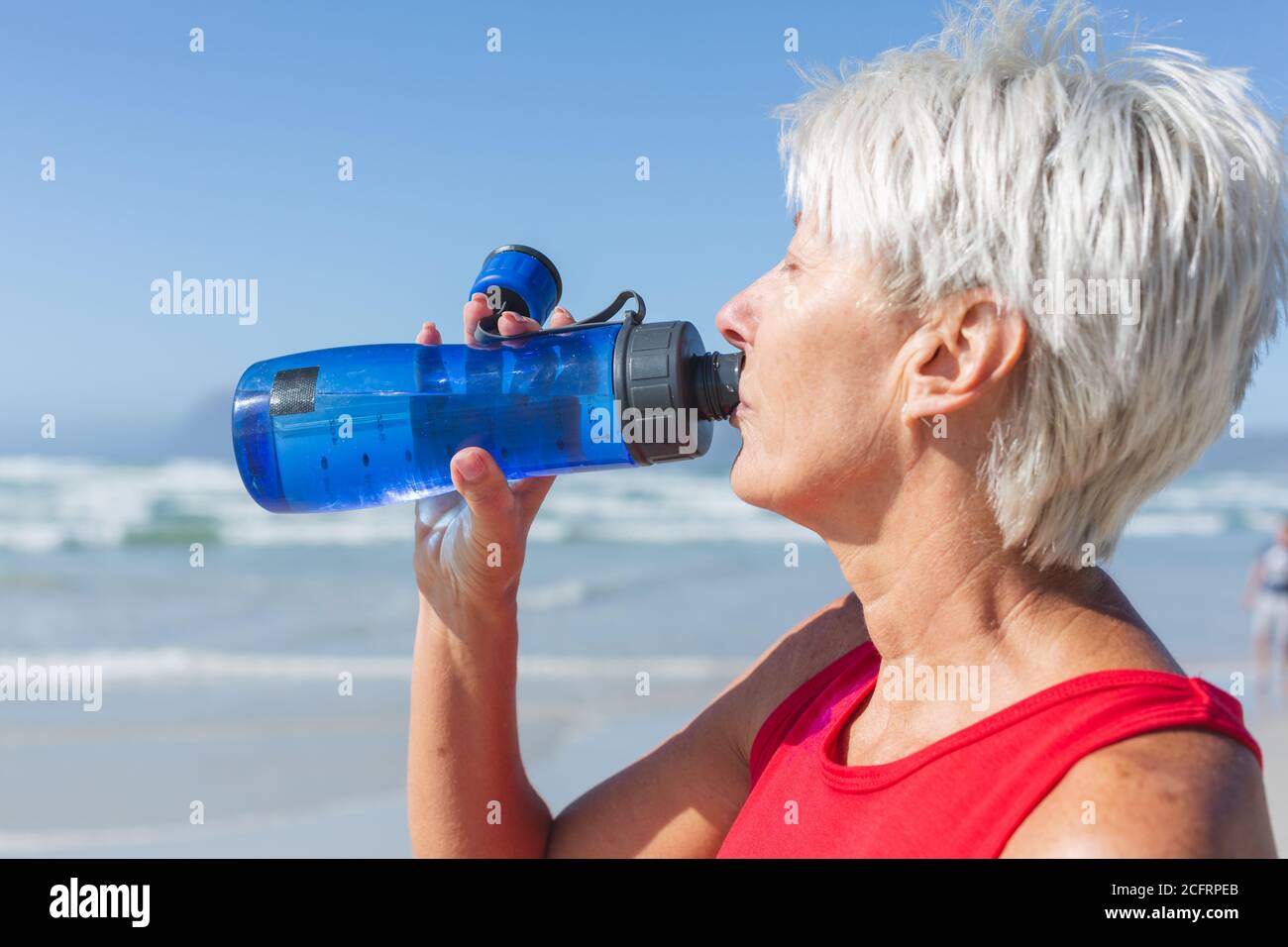 Femme âgée qui boit de l'eau à la plage Banque D'Images Femme âgée qui boit de l'eau à la plage Banque D'Images