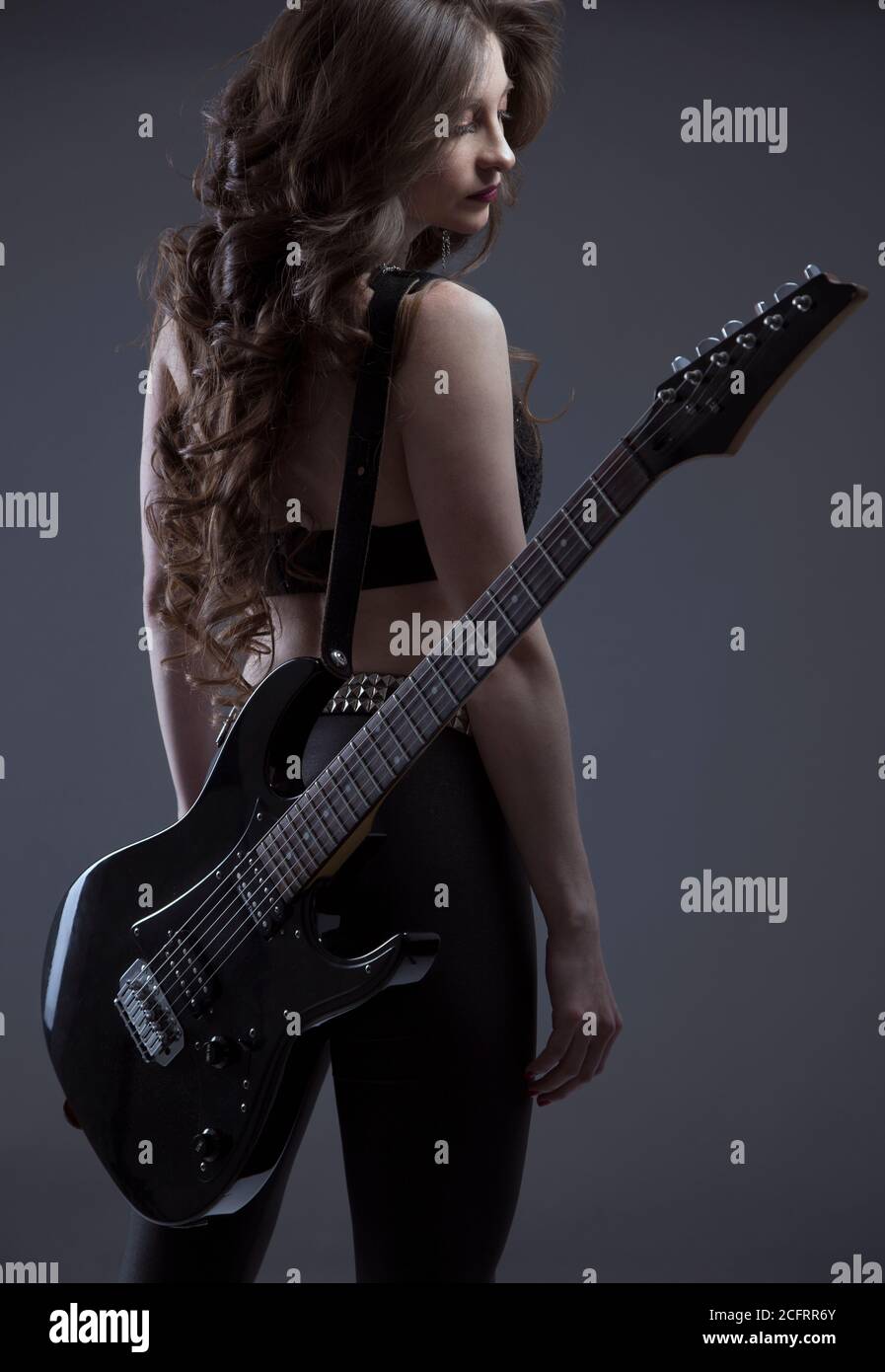 Jeune femme latine avec une peau blanche mince avec de longs cheveux, debout sur son dos avec une guitare électrique, portant le dessus et le pantalon noirs, studio Banque D'Images