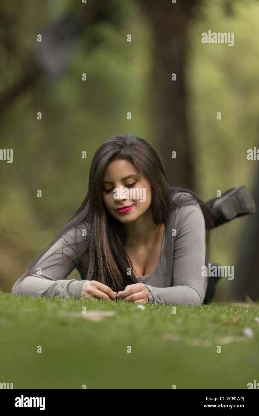 jeune femme à la peau blanche avec de longs cheveux et du maquillage est couché face vers le bas sur l'herbe avec ses mains vers le bas de son regard les regarder Banque D'Images