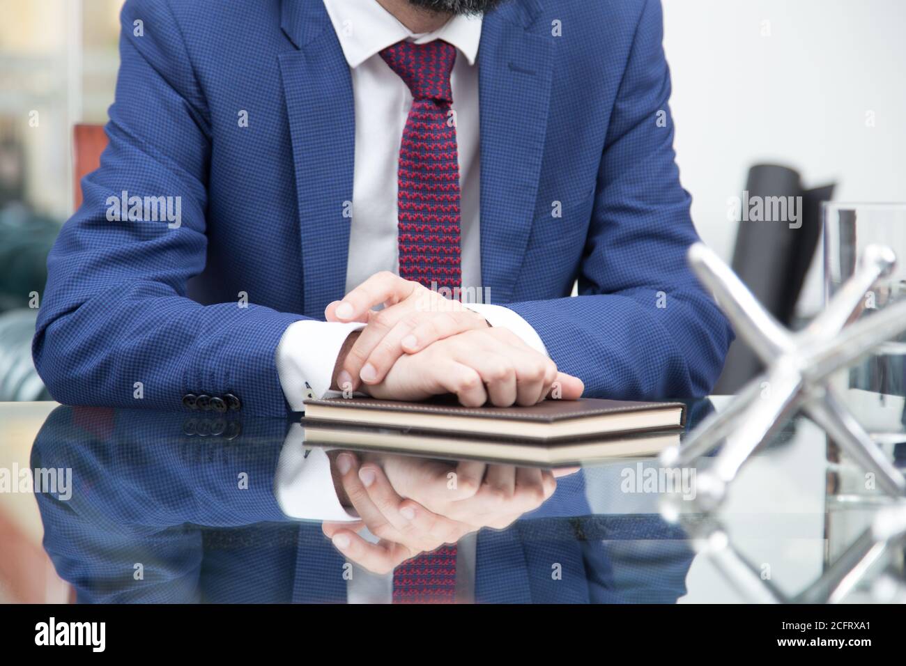 gros plan d'une personne avec un costume bleu, une cravate rouge et une  chemise blanche, assis sur un bureau en verre, pliant ses mains sur un  carnet marron Photo Stock - Alamy