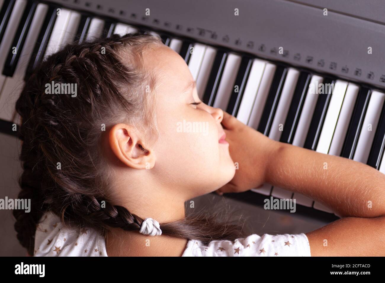 bébé fille en robe blanche dormant sur les clés du piano électronique, synthétiseur, gros plan Banque D'Images