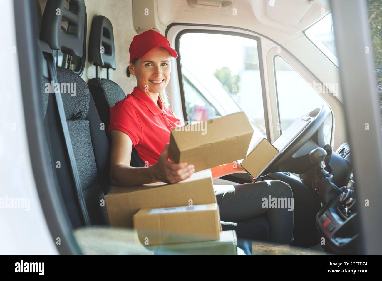 femme de service de livraison en uniforme rouge assis dans une camionnette avec des boîtes. souriant à la caméra Banque D'Images