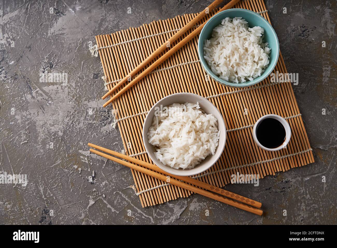 Riz dans un bol en porcelaine, avec baguettes japonaises, sauce soja, servi sur une table en pierre grise Banque D'Images