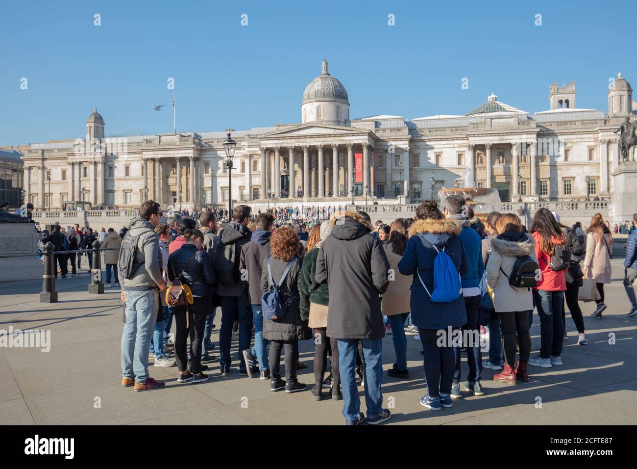 Grand groupe de touristes vus sur Trafalgar Square avec les bâtiments de la National Gallery of London vus sur fond bleu ciel. Banque D'Images