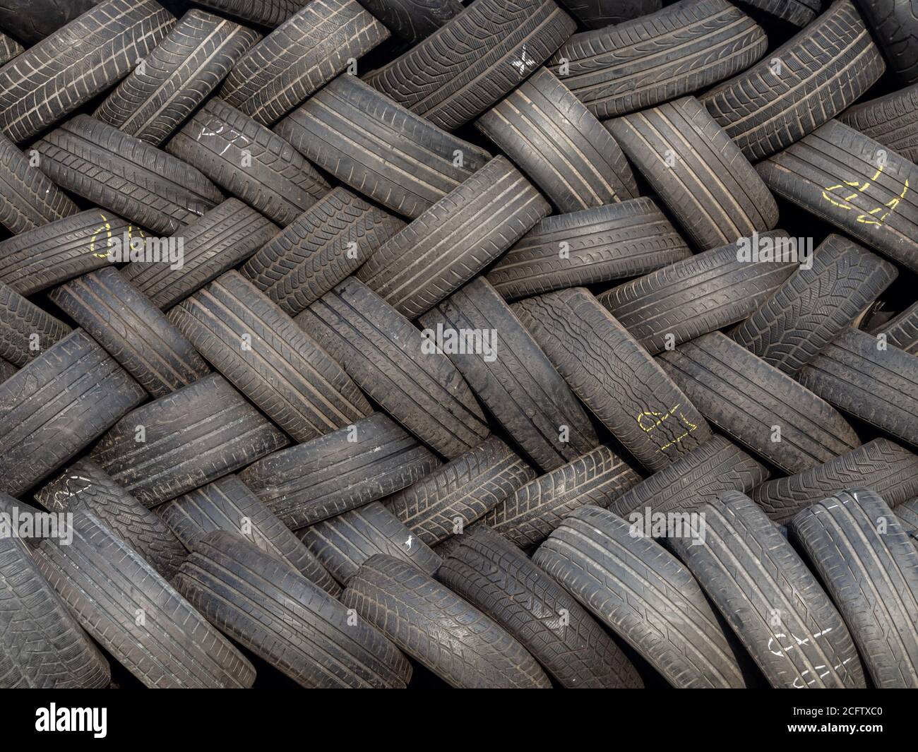 Photo conceptuelle montrant une pile de pneus de voiture d'occasion disposés selon un motif géométrique. Écologie, consumérisme, pollution, excès. Banque D'Images