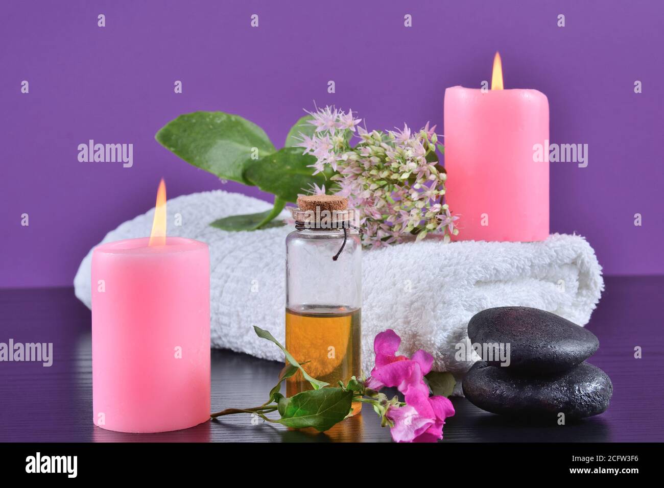 Décoration spa et bien-être sur un bureau avec bougies roses, serviette, huile aromatique et fleurs sur fond violet dans le studio Banque D'Images