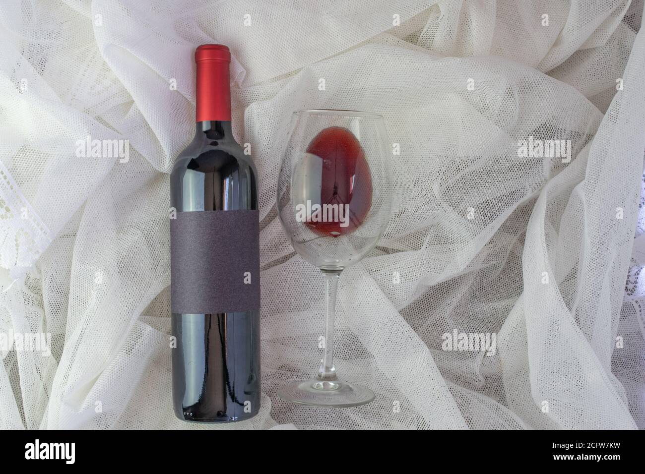 Composition romantique avec maquette de bouteille de vin rouge et verre de vin rouge sur tissu blanc dans la vue de dessus Banque D'Images