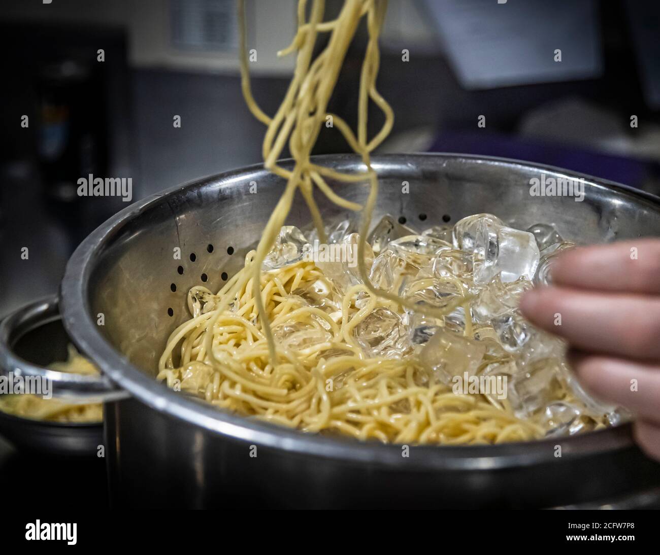 Un cuisinier refroidit des nouilles de riz fraîchement cuites dans un bain de glace dans la cuisine du True North au large d'Alor, Indonésie. Banque D'Images