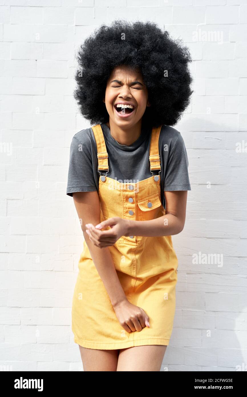 Drôle de dame africaine avec les cheveux afro riant debout contre le mur de brique blanche. Banque D'Images