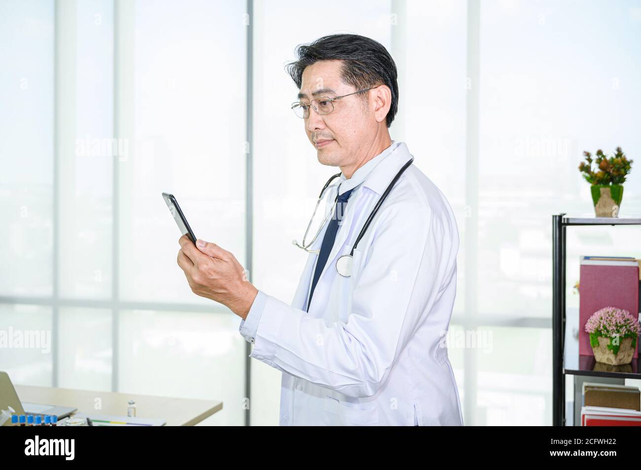 Asiatique adulte homme médecin portant un manteau blanc classique à l'aide d'un smartphone pour le service au travail. Spécialistes de la santé. Banque D'Images