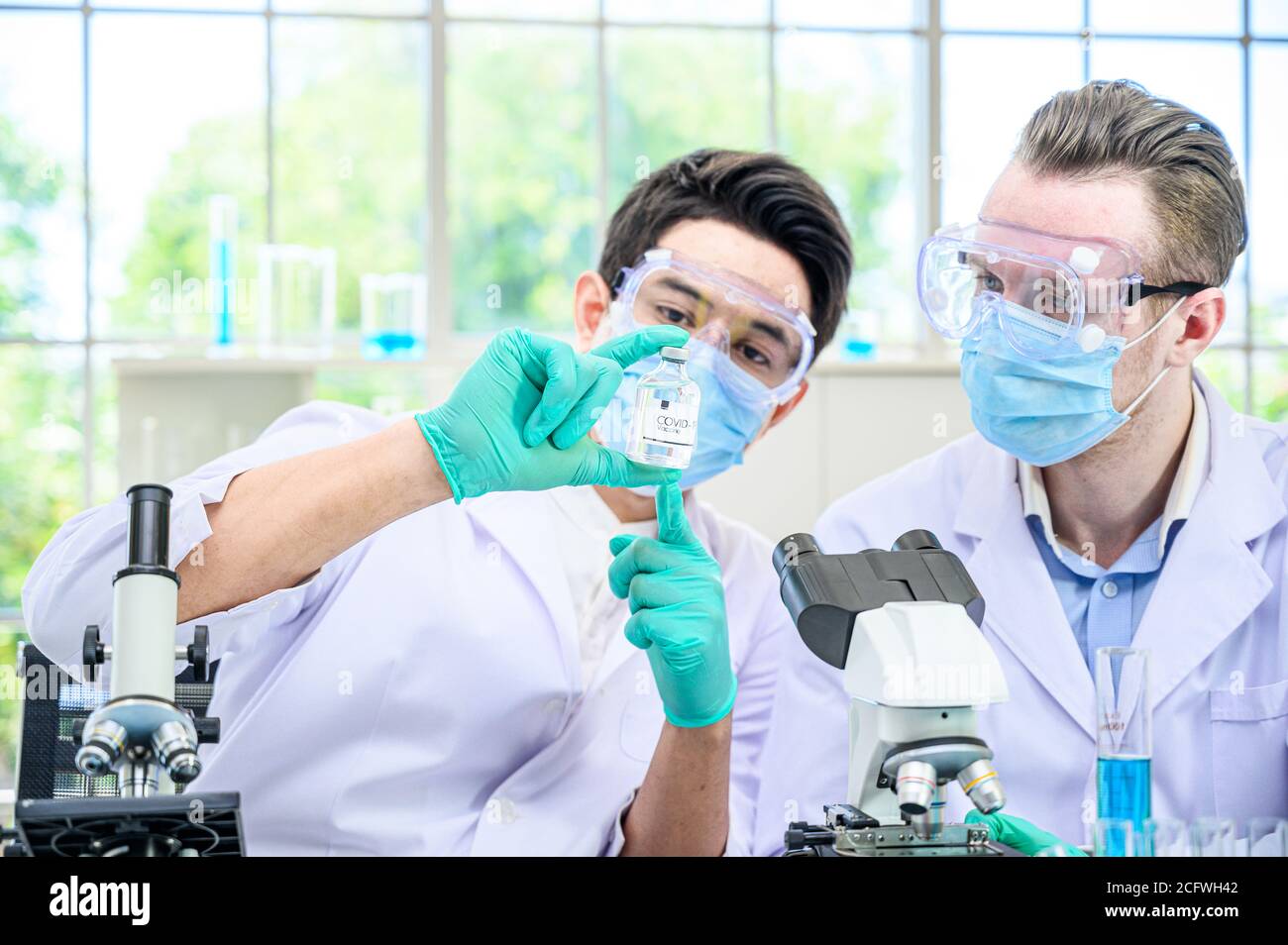 Couple de scientifiques mâles portant une combinaison de protection tenant le vaccin du coronavirus et travaillant avec de nombreux équipements de laboratoire pour la recherche de vaccins en laboratoire. Viru Banque D'Images