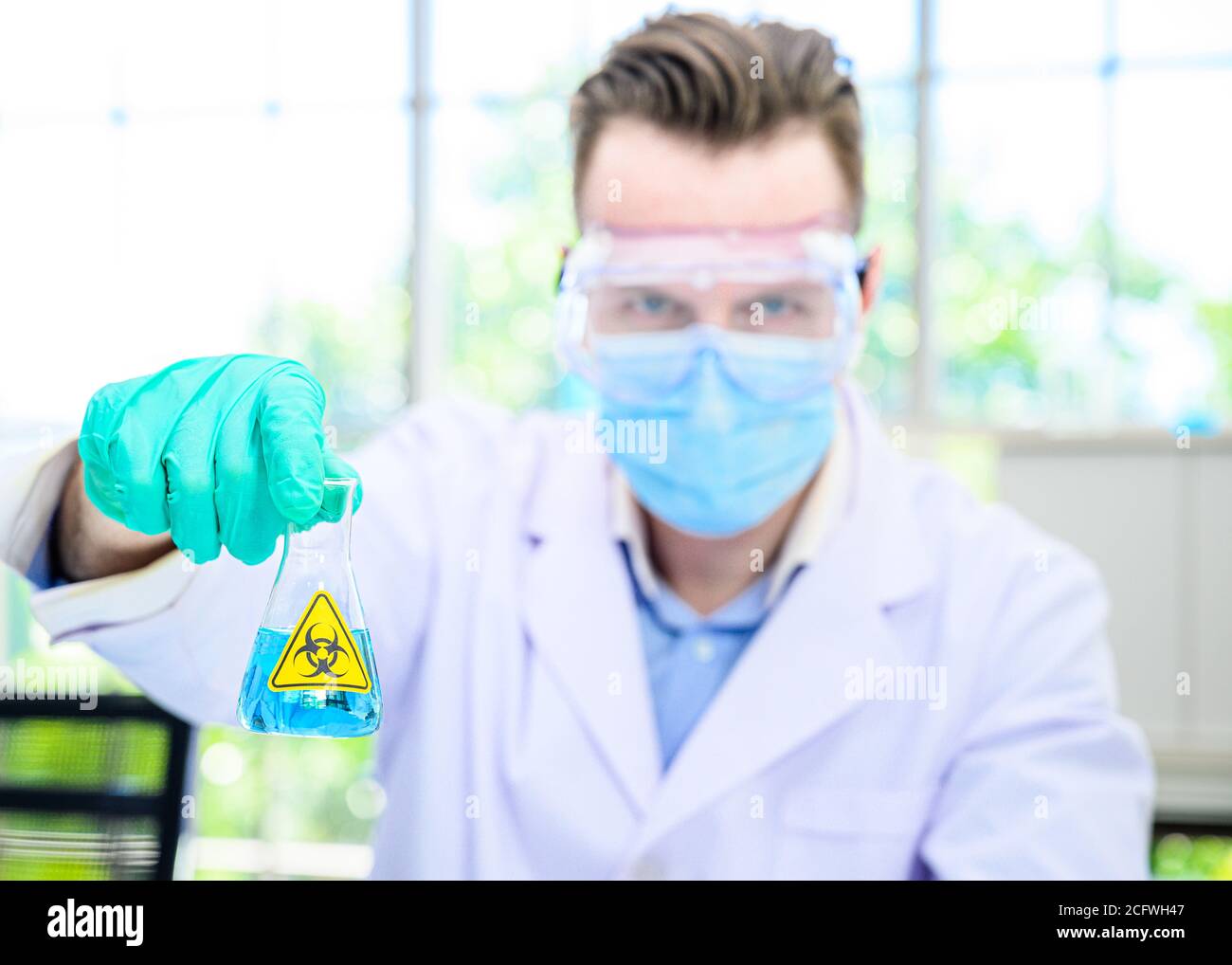 Un scientifique mâle porte une combinaison de protection pour le maintien d'un bécher ou d'un tube avec prélever du liquide à l'intérieur et travailler avec de nombreux équipements de laboratoire pour recherche en laboratoire Banque D'Images