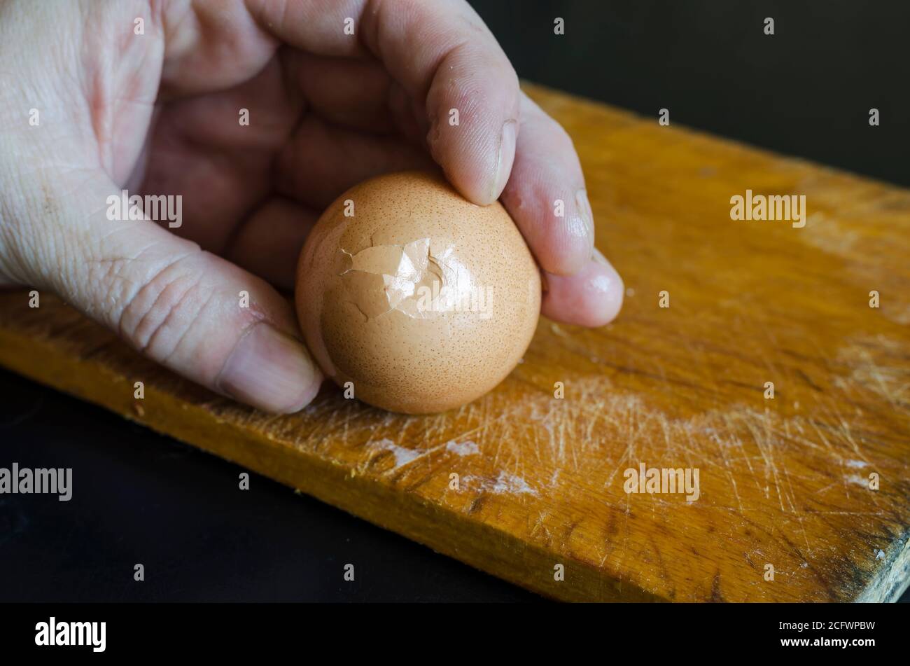 Une main mâle tient un œuf de poulet bouilli dans sa coquille contre la planche à découper. Méthode de nettoyage des coquilles. Cuisson. Mise au point sélective. Banque D'Images