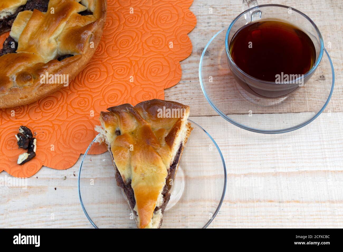 cuisine maison, une tarte, une tranche de tarte aux pommes remplie de cerises et de noix, une tasse de thé et une poignée de noix pelées sur une table en bois Banque D'Images