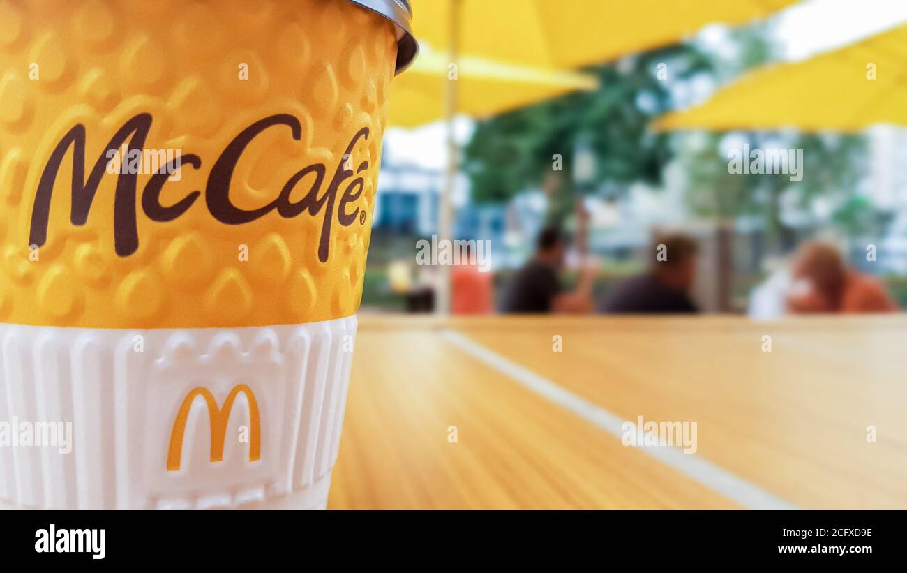 Menu McCafe au restaurant McDonalds. Une tasse de café jaune sur une table à l'extérieur avec des parasols jaunes et des visiteurs à l'arrière-plan. Petit déjeuner, café Banque D'Images