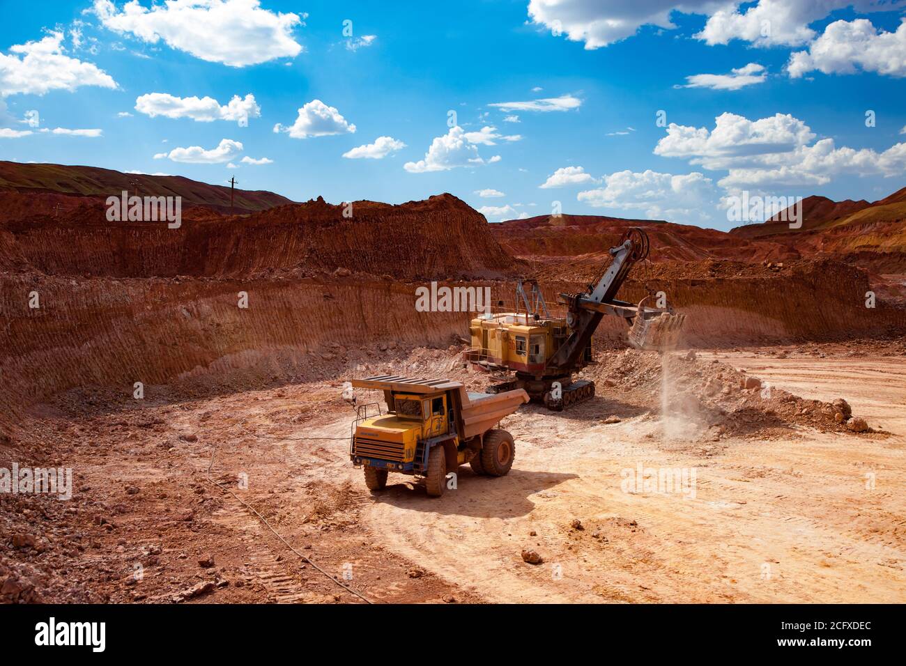 Exploitation et transport du minerai d'aluminium. Mine de bauxite à coupe ouverte. Pelle hydraulique de chargement de tombereau à benne basculante avec minerai. Ciel bleu avec nuage. Banque D'Images