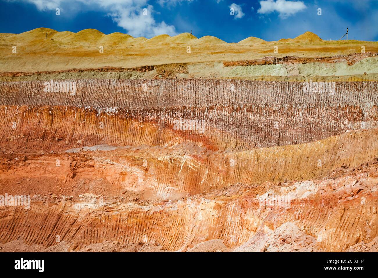 Carrière de minerai d'aluminium. Mine de bauxite à coupe ouverte. Texture de la coupe minérale avec le godet de pelle hydraulique. Couches de couleur du terrain. Sur un ciel bleu avec des nuages Banque D'Images