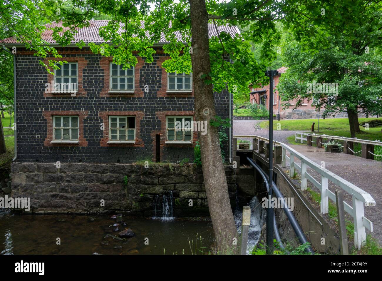 Village de Fiskars et son moulin en été. Ancienne usine de fer construite en brique de scories (construite en 1898). Quelques arbres et une rivière, Finlande. Banque D'Images