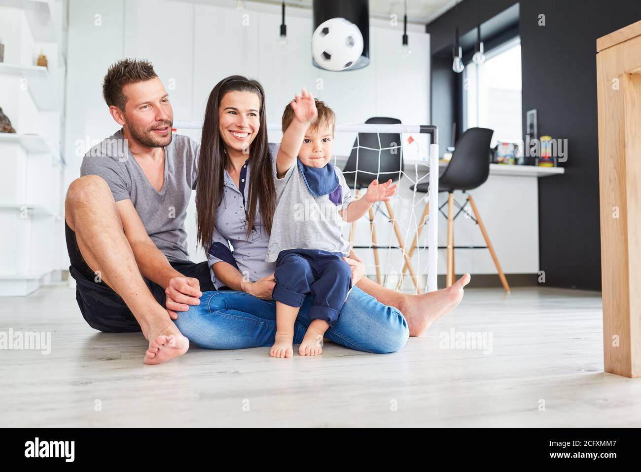 Tout-petit jette un ballon dans la salle de séjour tout en jouant avec les parents Banque D'Images