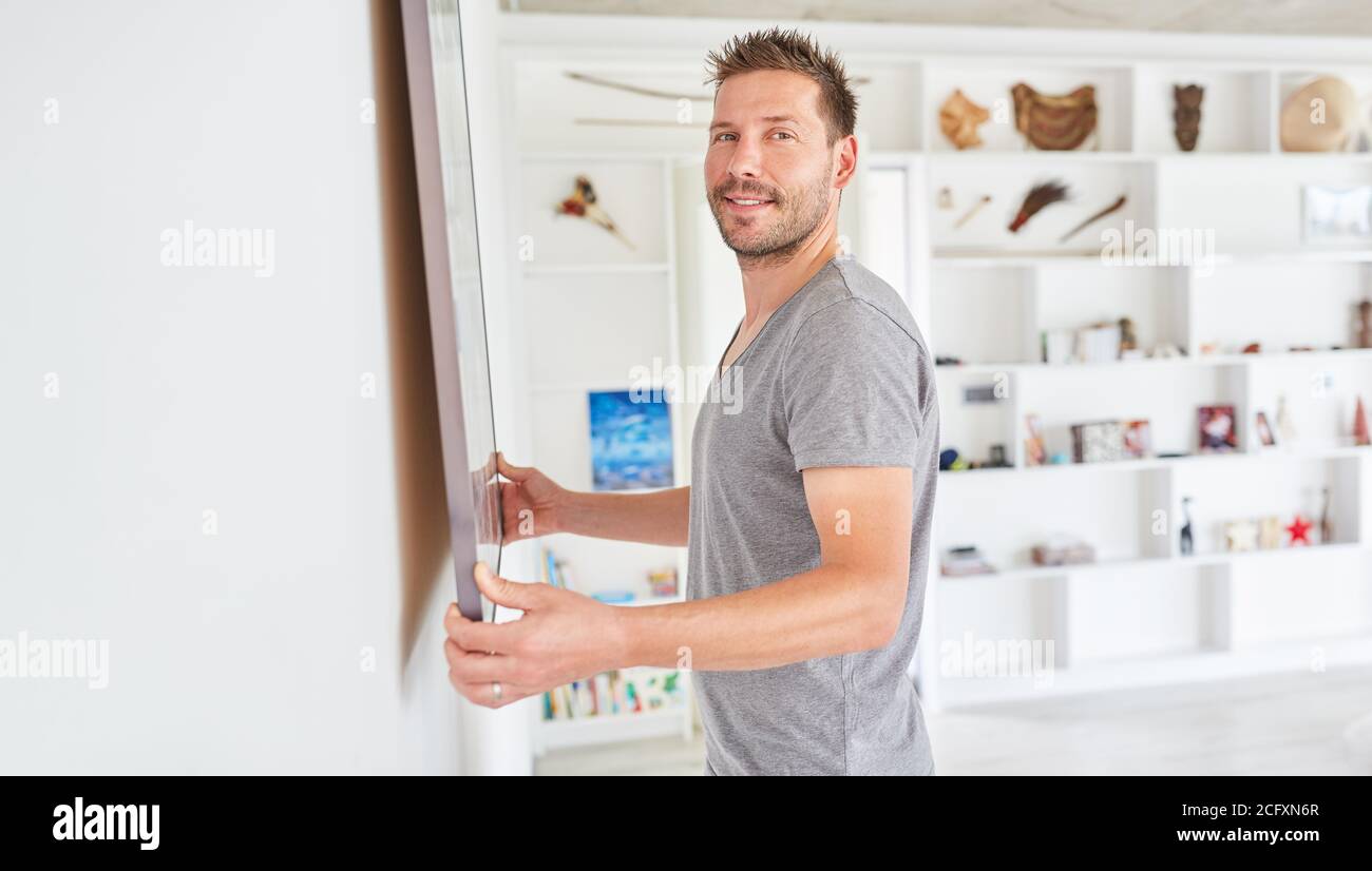 Un jeune homme pose une photo ou une photo sur un mur dans sa nouvelle maison Banque D'Images