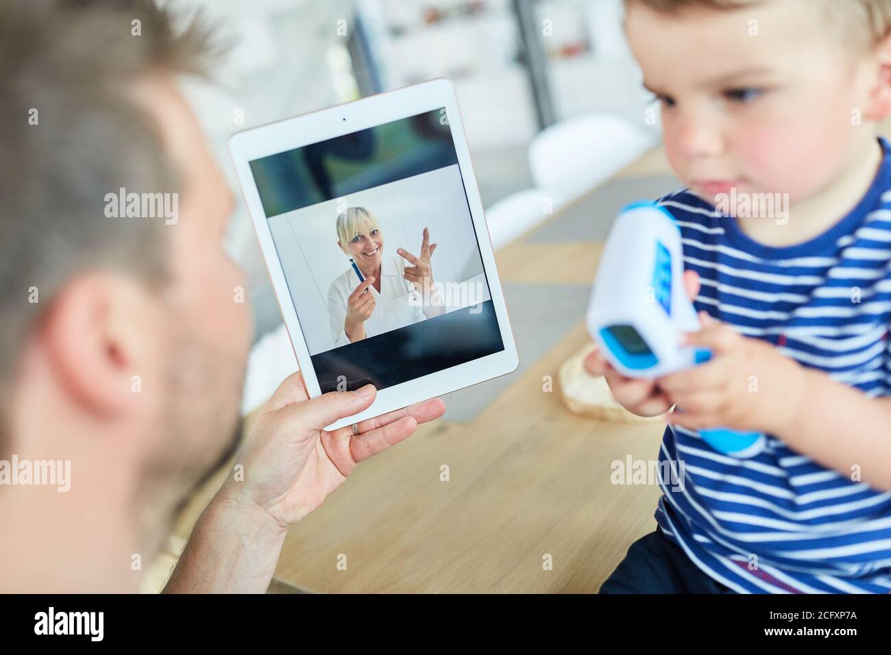 Père avec enfant mesurant la fièvre pendant la consultation en ligne par vidéo discutez sur une tablette Banque D'Images