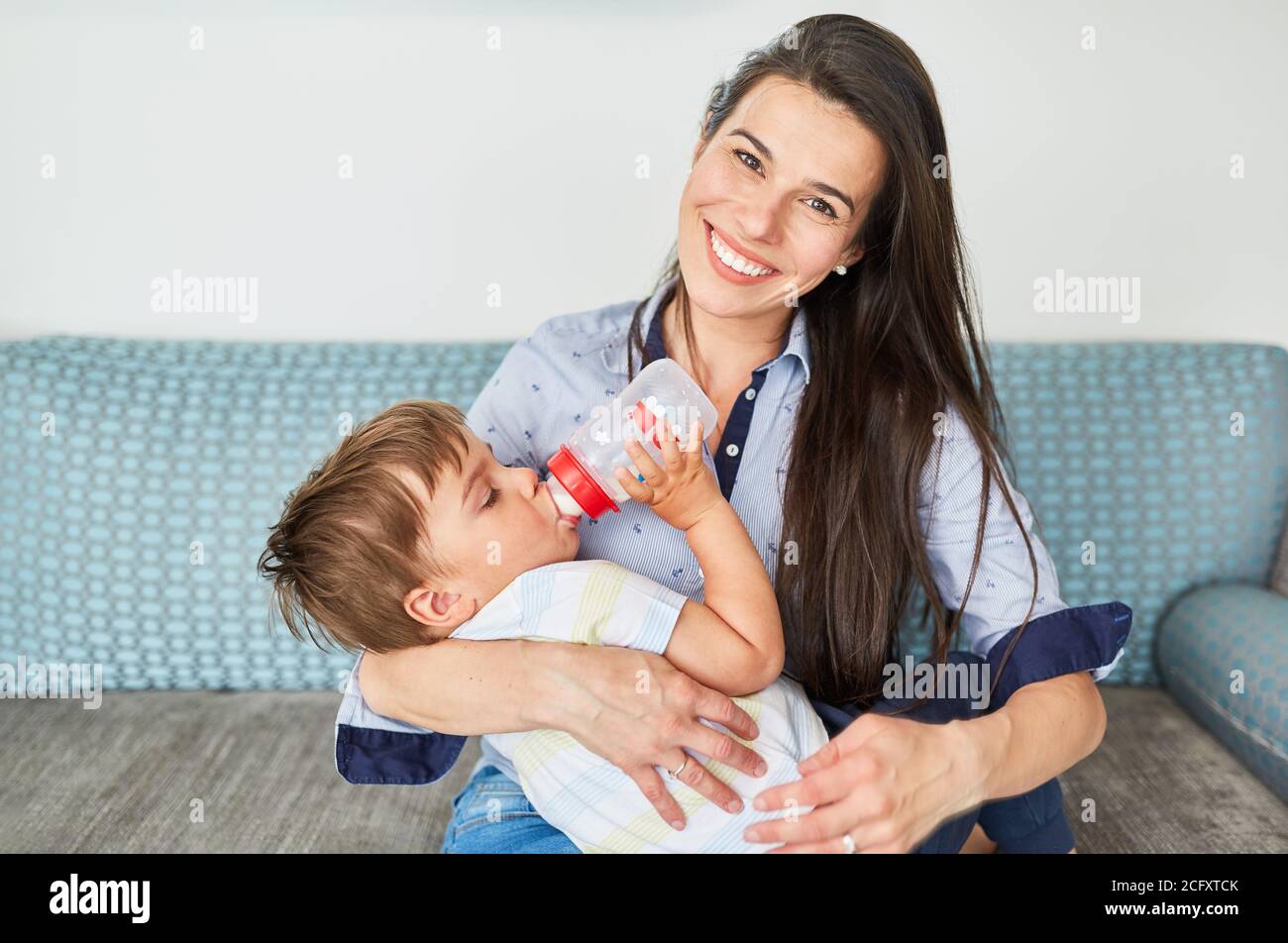 La Mere Tient Le Tout Petit Tout En Buvant Un Biberon De Lait Sur Le Canape Dans Le Salon Photo Stock Alamy