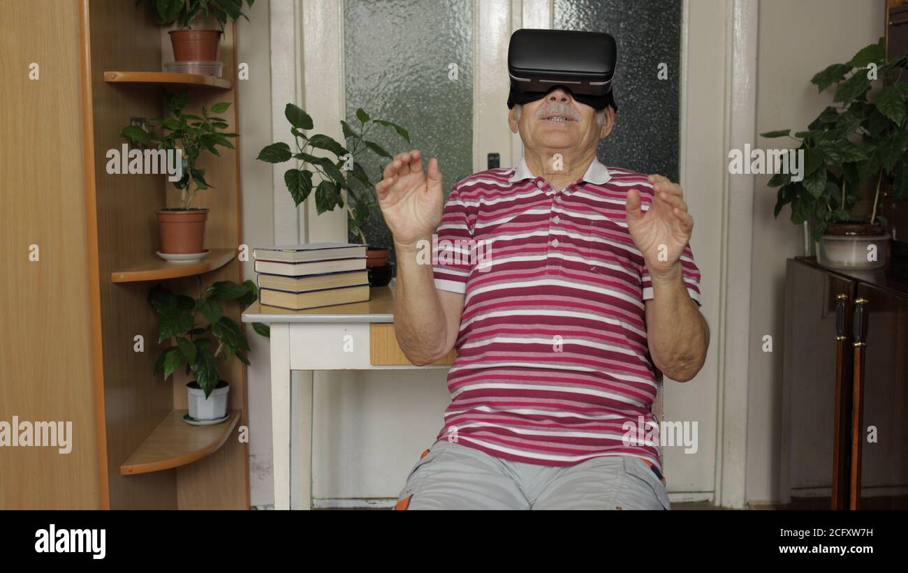 Grand-père émerveillé dans des lunettes de casque virtuel en regardant une vidéo  3D incroyable dans un casque VR 360 à la maison. Technologie future.  L'homme dans des lunettes VR jouant à des