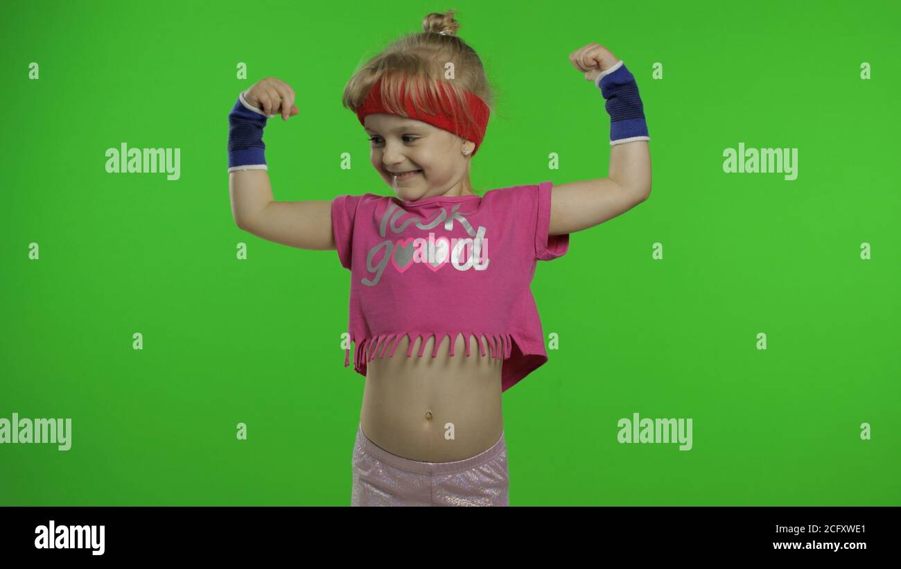 Petite fille caucasienne en rose sportswear faire des exercices de gymnastique à la maison de forme physique, montrant des muscles. Entraînement pour les enfants. Jeune enfant sportif dans la boîte d'entraînement de costume de sport, montre le combat de poing. Touche Chroma Banque D'Images