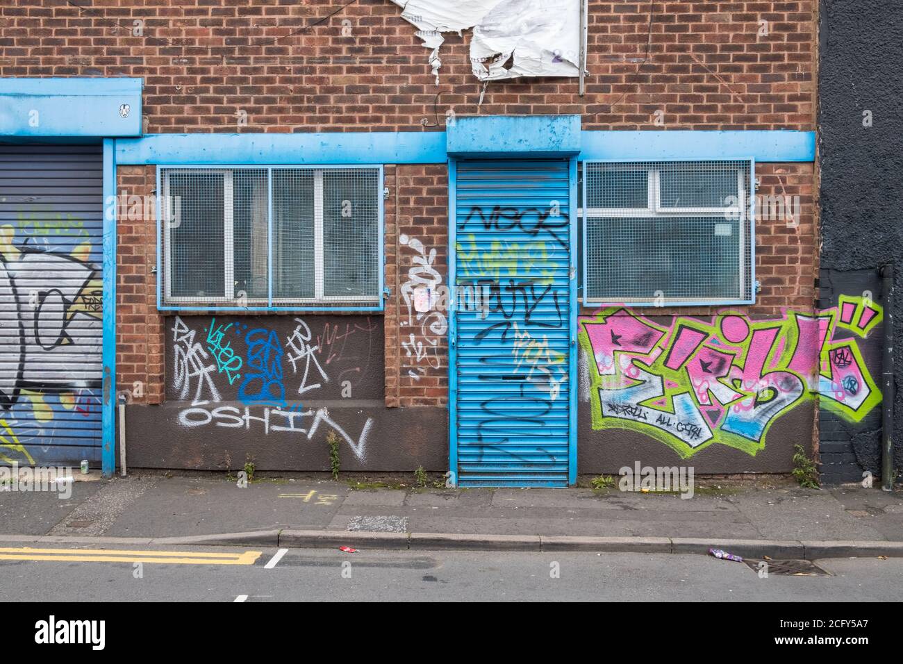 Petit atelier ou unité d'usine à Digbeth, Birmingham avec volets roulants bleus couverts de graffiti d'art de rue Banque D'Images